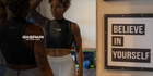 A confident individual dressed in athletic attire looking at themselves in a mirror, surrounded by motivational decor sign reading 'BELIEVE IN YOURSELF.' This image showcases the importance of self-appearance in fitness and bodybuilding.