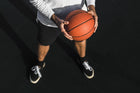 A basketball player holding an orange basketball with a determined posture, wearing a casual outfit, ready for training on the court.