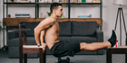 A man performing a chair dip exercise at home, showcasing a home gym setup with a modern couch and shelves in the background, emphasizing bodyweight training in a convenient workout space.