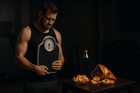 A concerned man holding a scale in front of a table with unhealthy snacks including chips, donuts, and soda. This image represents the struggle with fat loss and poor dietary choices.